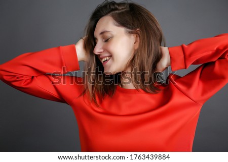 smiling sweet girl in red clothes. the young woman turned her head to the side with her eyes closed and smiles.