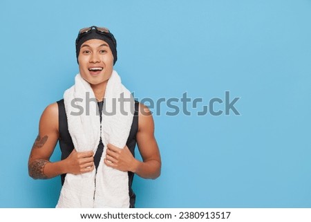 Smiling swimmer guy posing after swimming competition with towel on his neck and cap on his head, sport life concept, copy space.