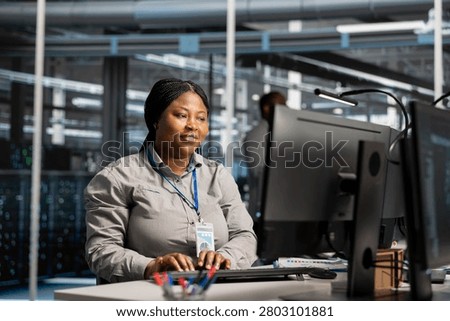 Smiling system administrator uses a computer to review server infrastructure, diagnostics and AI technology in a data center.