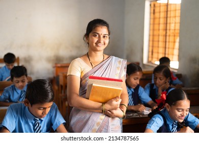 Smiling Teacher with books in hand standing at classroom in between students at classroom - concept of professional occupation, woman empowerment and education - Shutterstock ID 2134787565