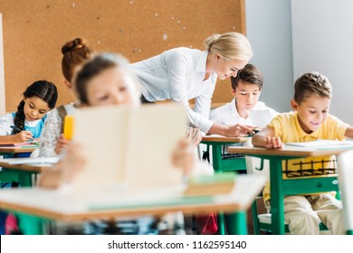 smiling teacher helping children with work during lesson