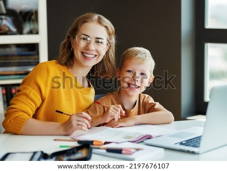 Smiling teacher or mother and schoolboy browsing laptop while doing assignment together and studying remotely at home