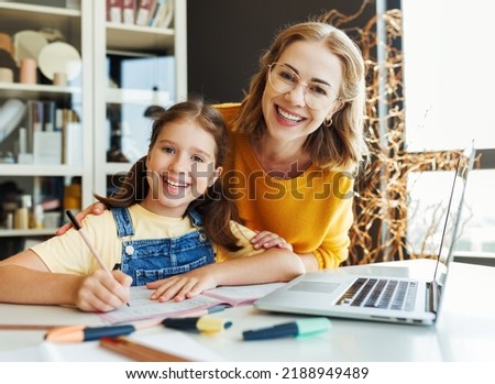 Smiling teacher or mother and schoolgirl browsing laptop while doing assignment together and studying remotely at home