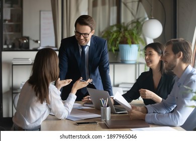 Smiling team leader with employees listening to businesswoman at corporate meeting, sitting in modern boardroom, happy colleagues partners discussing project strategy, sharing startup ideas - Shutterstock ID 1897965046