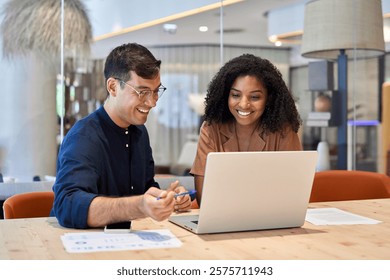 Smiling team professional employees working together on computer discussing online technology data solutions at work. Two young busy diverse coworkers business people using laptop at office meeting.