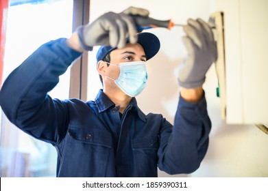Lächelnder Techniker repariert eine Warmwasserheizung mit einer Maske aufgrund einer Koronavirus-Pandemie