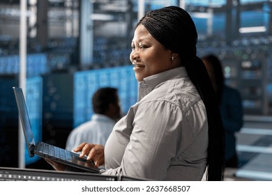 Smiling technician in server room using laptop to implement and manage data backup solutions. Happy data center engineer identifying and resolving technical issues, ensuring efficient recovery