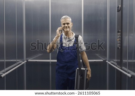 Smiling technician standing in the elevator and having a phone call, professional service and assistance concept