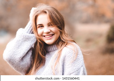 Smiling teen 14-16 year old wearing warm sweater outdoors. Looking at camera. Autumn season. 20s. 
