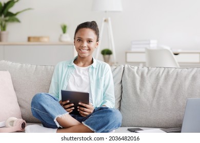 Smiling teen african american girl studying remotely, looking at camera, sits on sofa at home interior. Learn language online, lesson, modern instructional video and surfing in internet at free time - Powered by Shutterstock