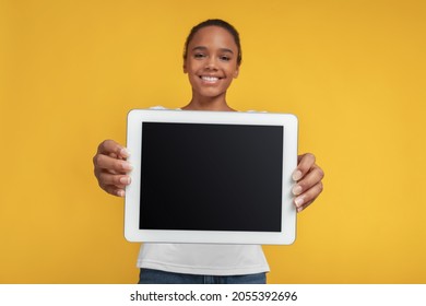 Smiling Teen African American Girl Show Tablet With Empty Screen, Isolated On Yellow Background. Student Advice, Website Ad And Online Study Remote. New Normal, App, Education And Social Networks