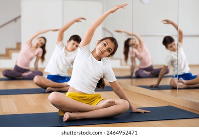 Smiling teen girl doing Padmasana with side stretch during yoga workout in gym with family.. - Powered by Shutterstock