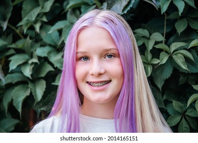 Smiling Teen Girl Wearing Dental Braces On Dark Green Leaves Background, Cute Caucasian Girl With Pink Hair Wearing Orthodontic Brackets