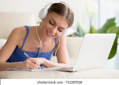 Smiling Teen Girl Wearing Headphones Listening To Audio Course Using Laptop At Home, Making Notes, Young Woman Learning Foreign Languages, Digital Self Education, Studying Online, Enjoying Music