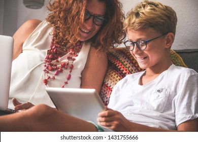 Smiling teen reading new trend stories online on tablet with mum. Technology addicted young boy watching social video at home with his mother. Child and mommy communicate and plays with tech device.