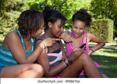 Smiling teenage black girls using a mobile phone at park