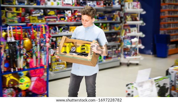 Smiling teenage boy choosing toy cement mixer\
machine in modern toy\
store