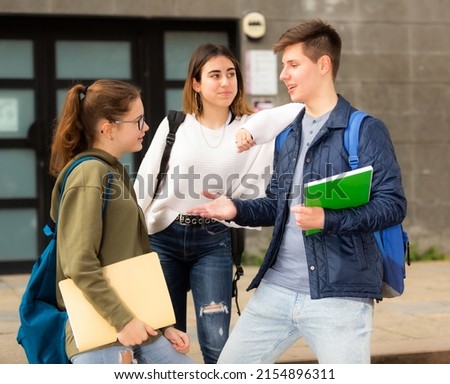Smiling teenage boy and girls with workbooks in hands socialize in the college yard