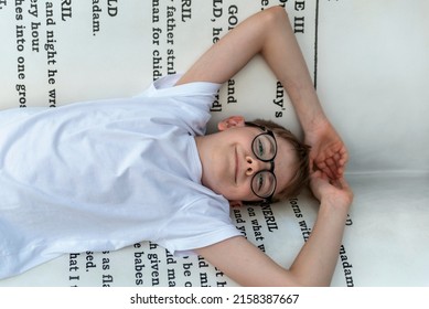 Smiling teenage boy with glasses lies on huge book. Bibliophile. Child loves to read. Literature in the school concept