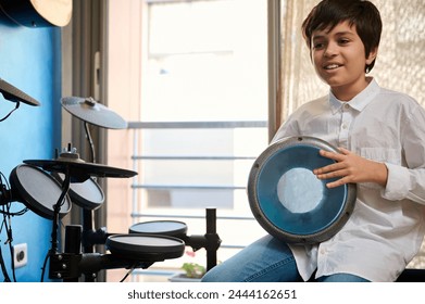 Smiling teenage boy musician enjoying playing the African ethnic percussion musical instrument drum - djembe, bongo, tam tam. Happy teenager creating the rhythm of African music banging ethnic drum - Powered by Shutterstock