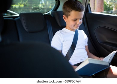 Smiling teenage boy reading book in the back seat of car - Powered by Shutterstock