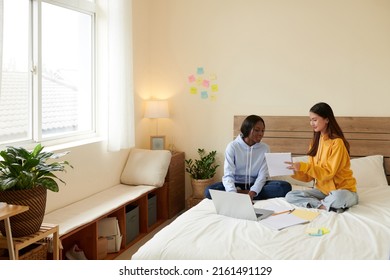 Smiling teenage girl explaining difficult topic to her friend and helping with doing homework