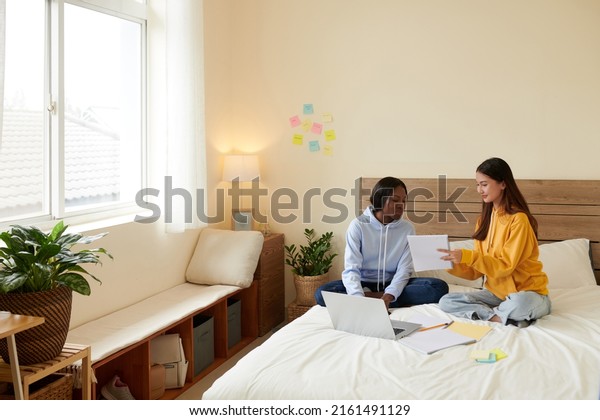 Smiling teenage girl explaining\
difficult topic to her friend and helping with doing\
homework
