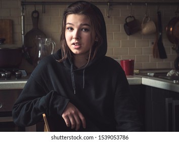 Smiling Teenage Girl In A Jacket With A Hood At Home In A Dark Room, Real People Every Day Life