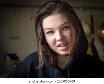 Smiling Teenage Girl In A Jacket With A Hood At Home In A Dark Room, Real People Every Day Life