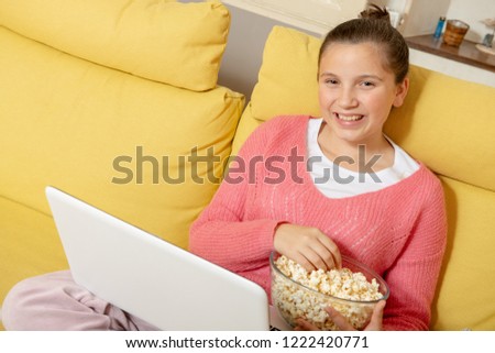 a smiling teenage girl using a laptop and eating popcorn