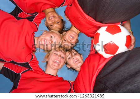 Smiling teenage girls in soccer team uniforms in huddle at camera