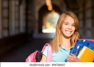 Smiling Teenage Schoolgirl With Books And Bookbag In Outdoor Campus Hallway