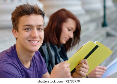 Smiling teenage student outdoors with a girl at the background