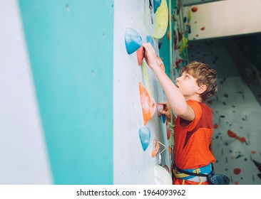 Smiling teenager boy at indoor climbing wall hall. The boy is climbing using a top rope and climbing harness. Active teenager time spending concept image - Powered by Shutterstock