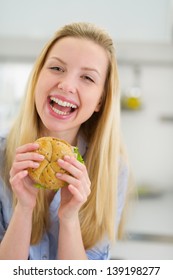 Smiling Teenager Girl Eating Sandwich In Kitchen