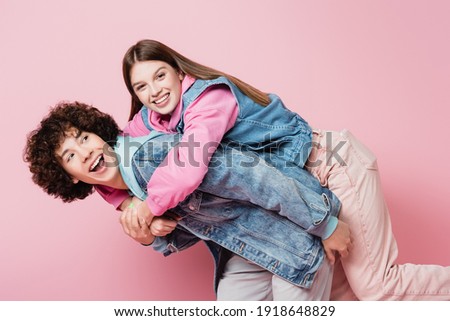 Smiling teenager piggybacking on boyfriend isolated on pink