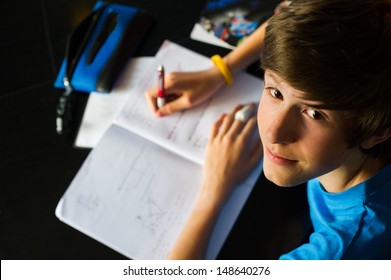 Smiling teenager studying and doing his homework while holding his pen and writing in his notebook. 