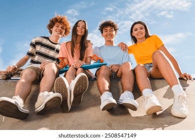 Smiling teenagers high school pupils friends classmates college students boys girls sitting on ramp skating in skate park spending good time summer holiday weekend having fun hanging out together - Powered by Shutterstock