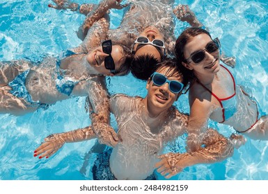 Smiling teenagers in swimsuits and sunglasses swim in the pool. A joyful group of friends is having fun in the clear water. Cute boys and girls are enjoying their holidays together. - Powered by Shutterstock