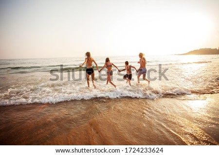 Smiling teens run on vacation. Happy young people having fun at beach on sunny day.