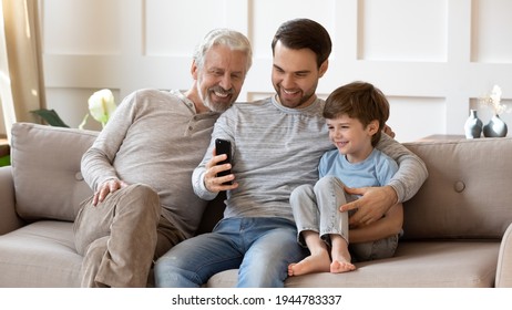 Smiling three generations of men sit rest on sofa in living room talk on video call on smartphone gadget. Happy little Caucasian boy child with father and grandfather use modern cellphone at home. - Powered by Shutterstock