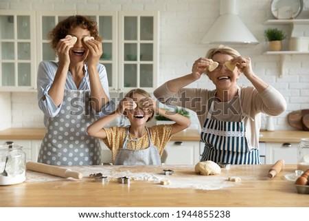 Smiling three generations of woman have fun baking sweet cookies dessert at home together. Portrait of overjoyed little girl child with young mother and mature grandmother cooking in kitchen.