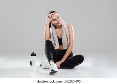 Smiling Tired Young Woman Athlete With Towel And Bottle Of Water Over Gray Background