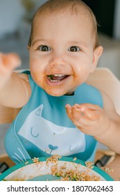 Smiling Toddler Girl Eating Rice And Have Fun During Her Meal. Close Up Of Hispanic Toddler's Face With Tomato Sauce.