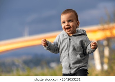 Smiling toddler in a grey hoodie enjoying a playful moment outside. The child exhibits joy and happiness while exploring nature in Mission, BC, Canada. - Powered by Shutterstock