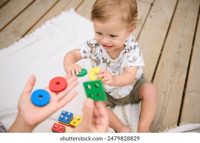 Smiling toddler playing with colorful educational toys on a wooden deck, engaging in fun indoor activities and learning shapes. - Powered by Shutterstock