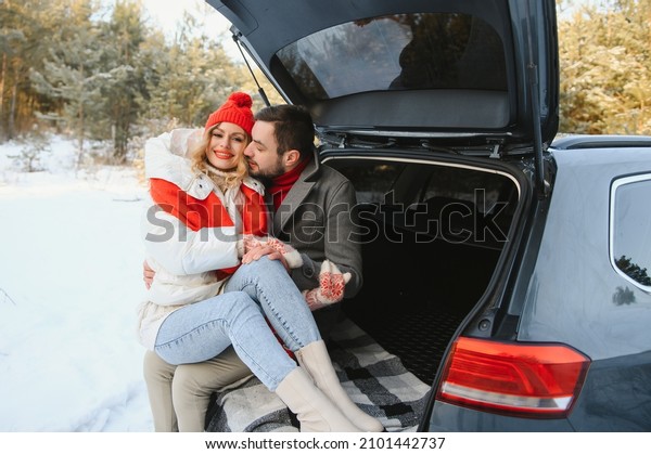 Smiling together.\
Nice couple have weekend at countryside at winter time. Sitting on\
the rear part of modern\
car.