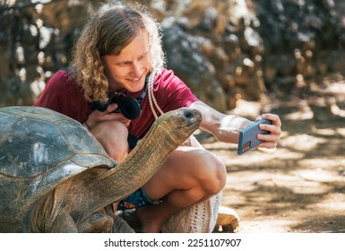 Smiling tourist boy making a selfie using cell phone with Aldabra giant tortoise endemic species - one of the largest tortoises in the world in the zoo nature park on Mauritius island. - Powered by Shutterstock