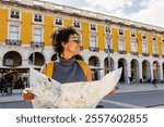 Smiling tourist is holding a map and wearing a yellow backpack while visiting the beautiful city of lisbon in portugal during summer vacations