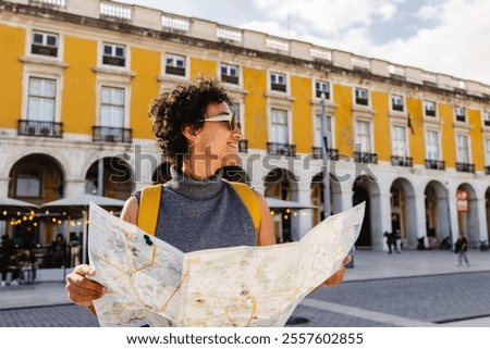 Smiling tourist is holding a map and wearing a yellow backpack while visiting the beautiful city of lisbon in portugal during summer vacations